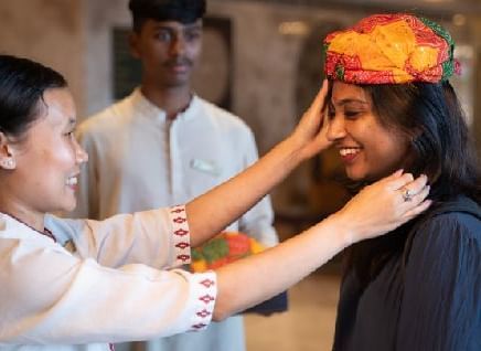 A woman welcoming a guest in a traditional Rajasthani way by placing a hat on her head - Kaldan Samudra Palace